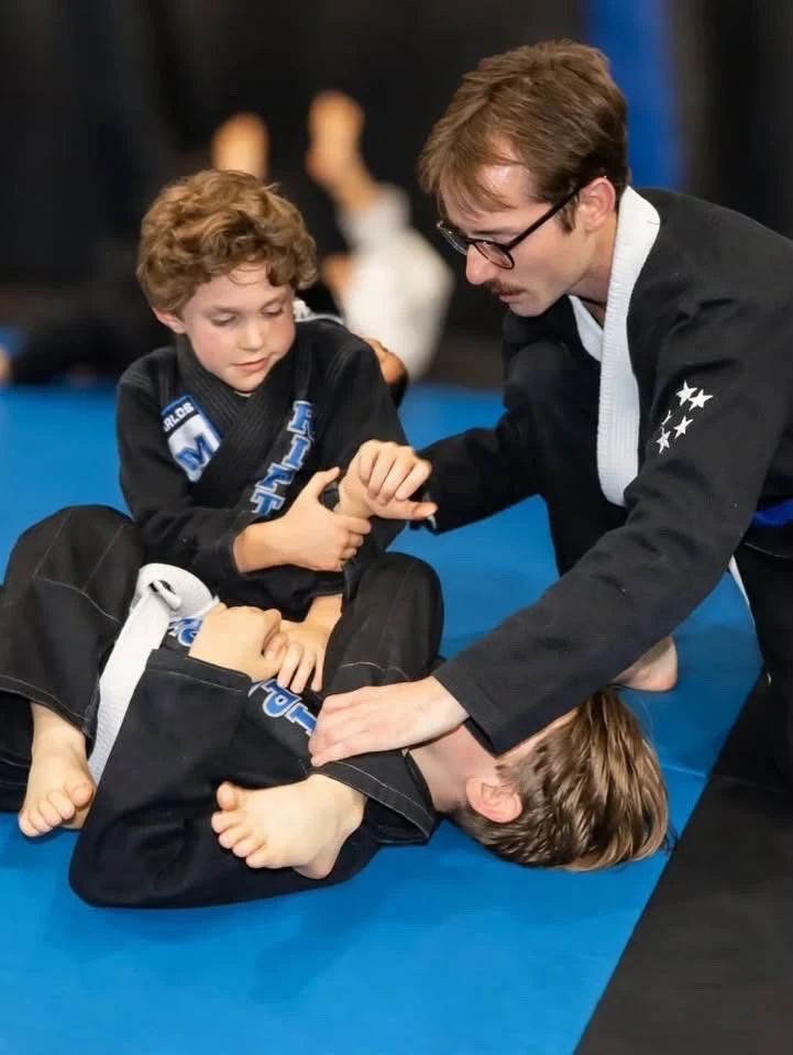 Coach Nathan guiding young students through a Jiu-Jitsu technique